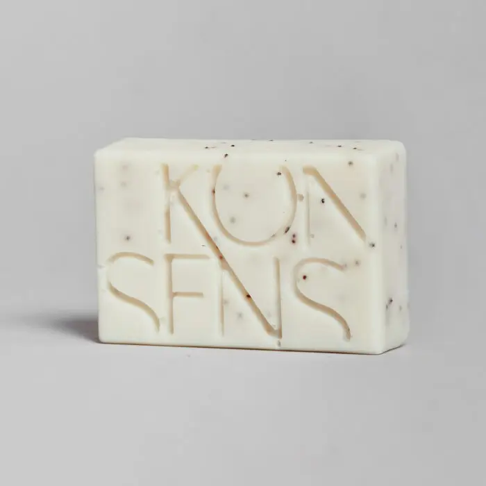 KONSENS Anti-Akne Seife auf neutralem grauen Hintergrund, zeigt das Konsens-Logo und enthält feine Peelingpartikel zur Reinigung und Pflege unreiner Haut.
