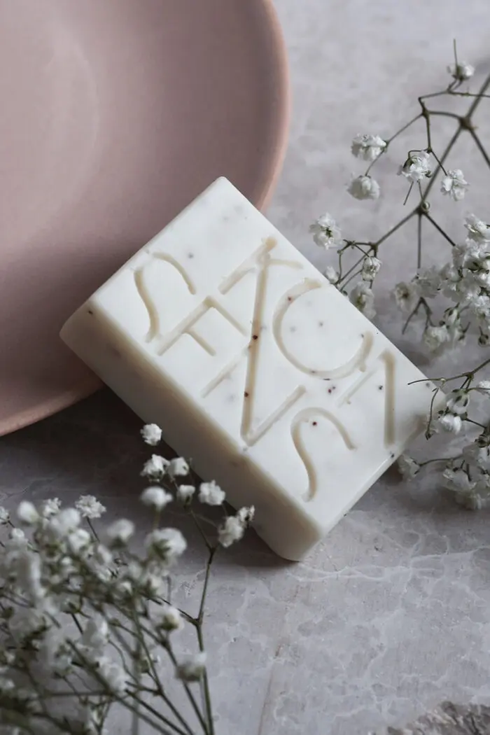 Weisse KONSENS Anti-Akne Seife auf hellem Untergrund, verziert mit kleinen Blüten. Die Seife zeigt das Konsens-Logo und ist für die Behandlung von Akne und unreiner Haut geeignet. Erhältlich bei Mel’s Beauty & Academy.