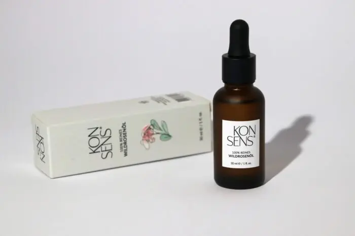 “Flasche mit 100% reinem Wildrosenöl von Konsens, präsentiert neben der eleganten Verpackung, die auf einer Seite liegt. Erhältlich bei Mel’s Beauty & Academy.”